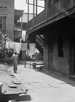 Clothes Line Prints: Man standing in a courtyard, New Orleans, between 1920 and 1926. Creator: Arnold Genthe