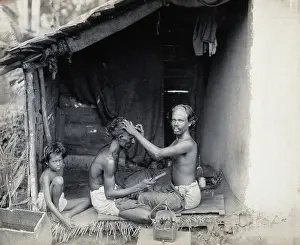 Sitting On Ground Prints: Two men sitting cross-legged; one is a barber shaving the front of the other's head