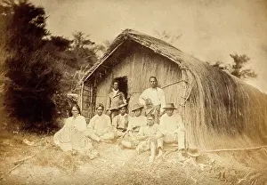 Sitting On Ground Prints: New Zealand: a group of Maori sitting in front of a traditional house