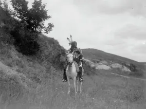 Sioux Indian on horseback, wearing two feathers, beaded buckskin shirt, and leggings... c1907. Creator: Edward Sheriff Curtis