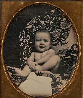 [Smiling, Nude Baby Holding Foot, Seated on Furniture Draped with Floral Print Fabric]