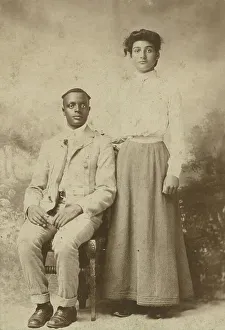 Studio portrait of a young couple, he seated, she with hand on his shoulder, c1900. Creator: Carbon Studio
