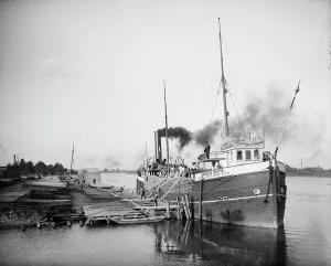 Black Smoke Prints: Unloading lumber, Saginaw, Mich. between 1900 and 1910. Creator: Unknown