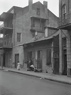 French Quarter Prints: View from across street of a man and child sitting on steps and a woman walking down