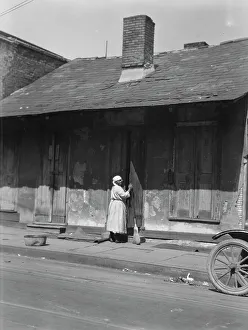 View from across street of a woman with a broom standing in a doorway, New Orleans, c1920-c1926. Creator: Arnold Genthe