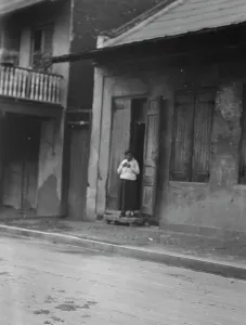 French Quarter Prints: View from across street of a woman standing in a doorway in the French Quarter