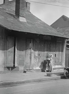 French Quarter Prints: Woman holding a sack standing by the doorway of a building in the French Quarter