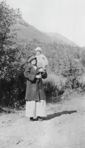 Settlers Prints: Woman standing on dirt road holding child; mountains in background