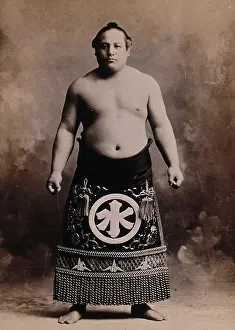A young sumo wrestler posing in a photographic studio, wearing a richly decorated apron... c1900. Creator: Unknown