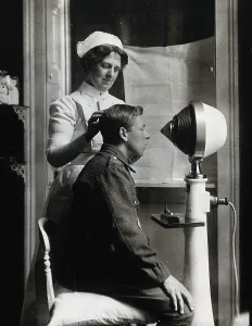 A young uniformed man sitting with a pillow on his chair, facing a machine... c1910s. Creator: Unknown